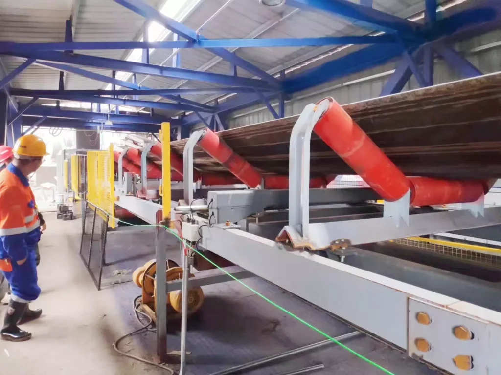 In an industrial site, a worker checks a belt scale system with red belt scale rollers, crucial for accurate bulk material measurement.
