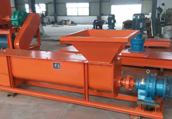 An orange U-shaped screw feeder (open trough screw conveyor) with a hopper and motor, featured in an industrial workshop. Its open square trough design allows for easy cleaning and maintenance, making it suitable for scenarios with large material flow and easy residue accumulation.