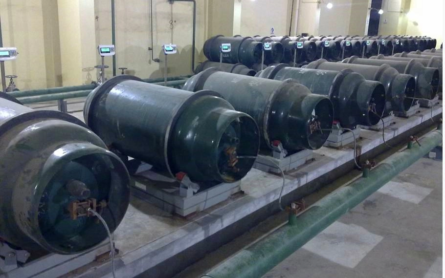 Multiple large gas cylinders sit on cylinder scales with electronic displays in an industrial facility.